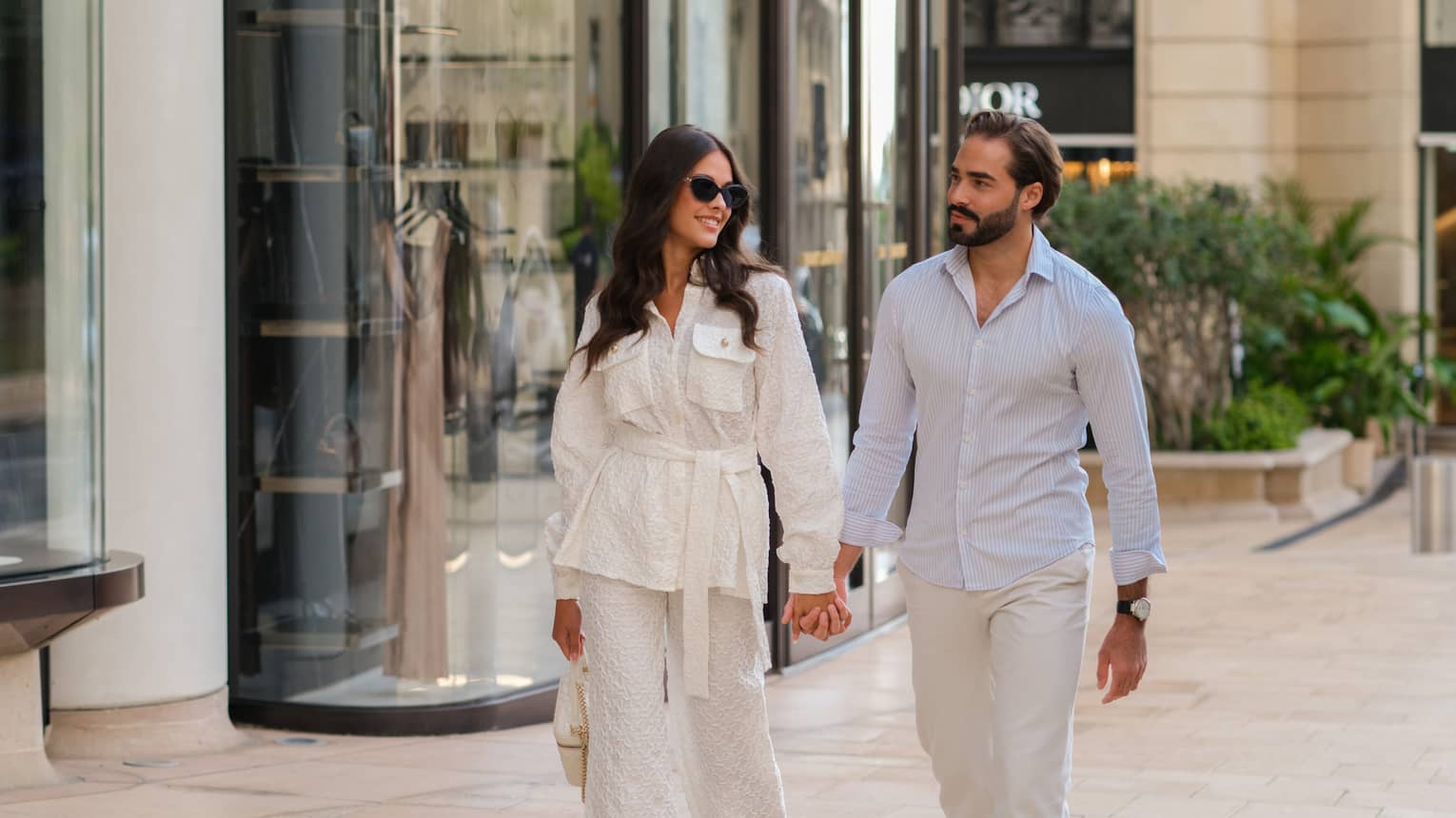 A couple holding hands while walking down a city street filled with shops
