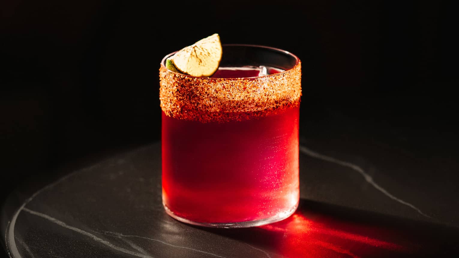 Red tequila-based cocktail served in a rocks glass and garnished with a lime wedge