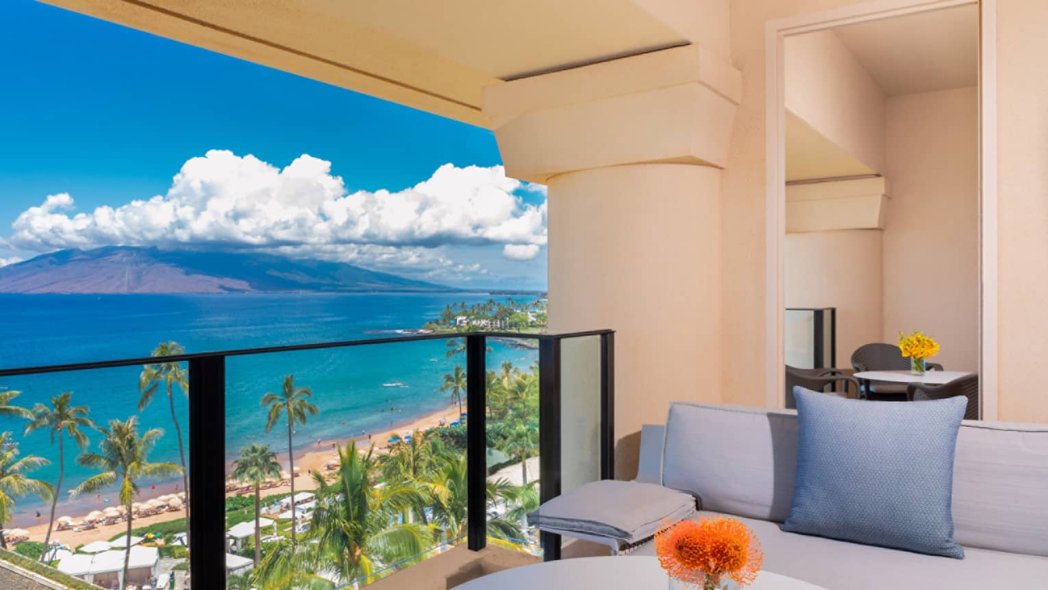 Balcony with cushioned seating, ocean and beach view palm trees and mountains under a bright blue sky