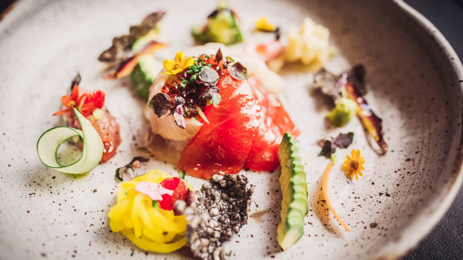 Close-up of gourmet sashimi plate garnished with greens, vegetables, puffed rice