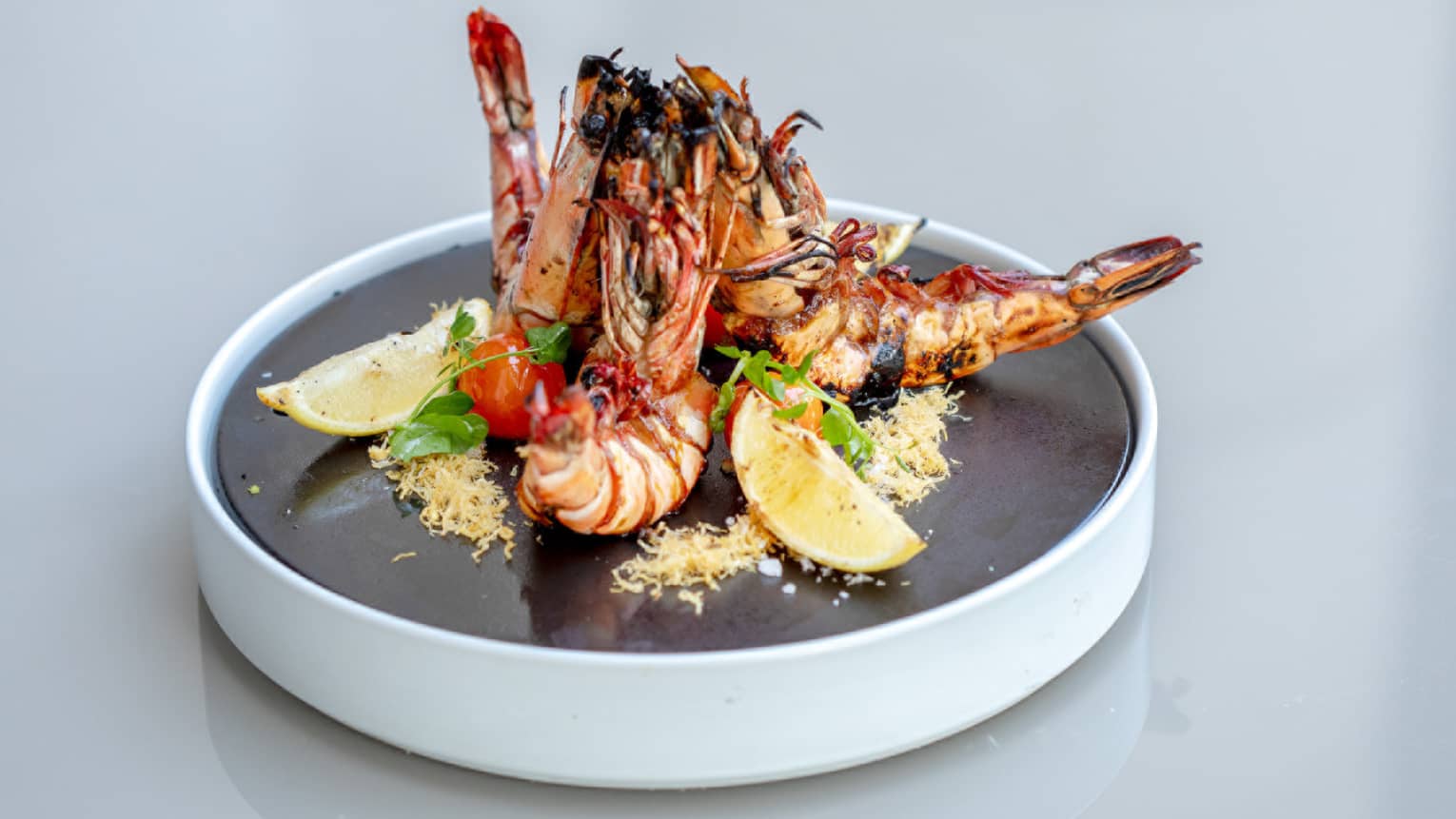A plate of prawn with sliced lemon served on a black platter.
