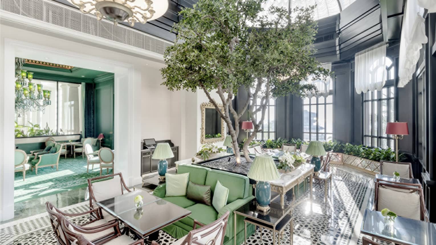 A lounge with a several square tables, and a live tree in the centre of the room.