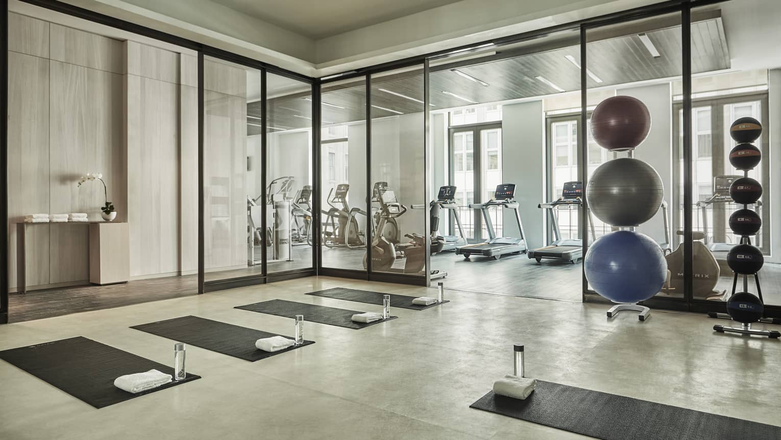 Yoga mats and water bottles in rows on Fitness Centre flow, stack of pilates balls
