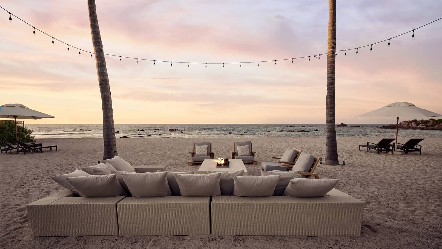 Coral Beach House sectional sofa and firepit on the beach, string lights, palm trees