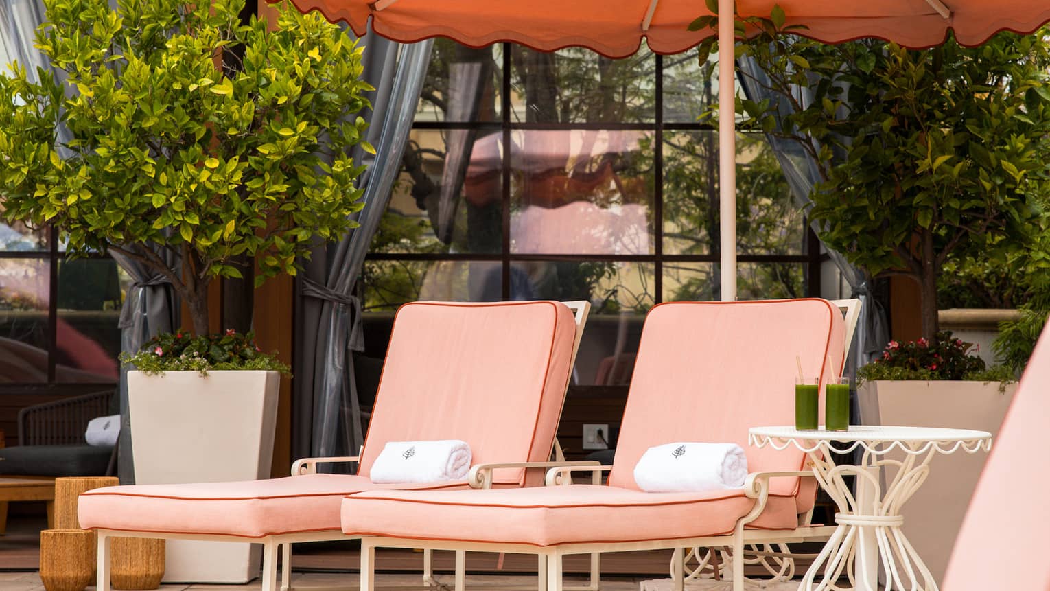 Pink lounge chair set beneath a pink scalloped-edge umbrella next to a row of poolside cabanas