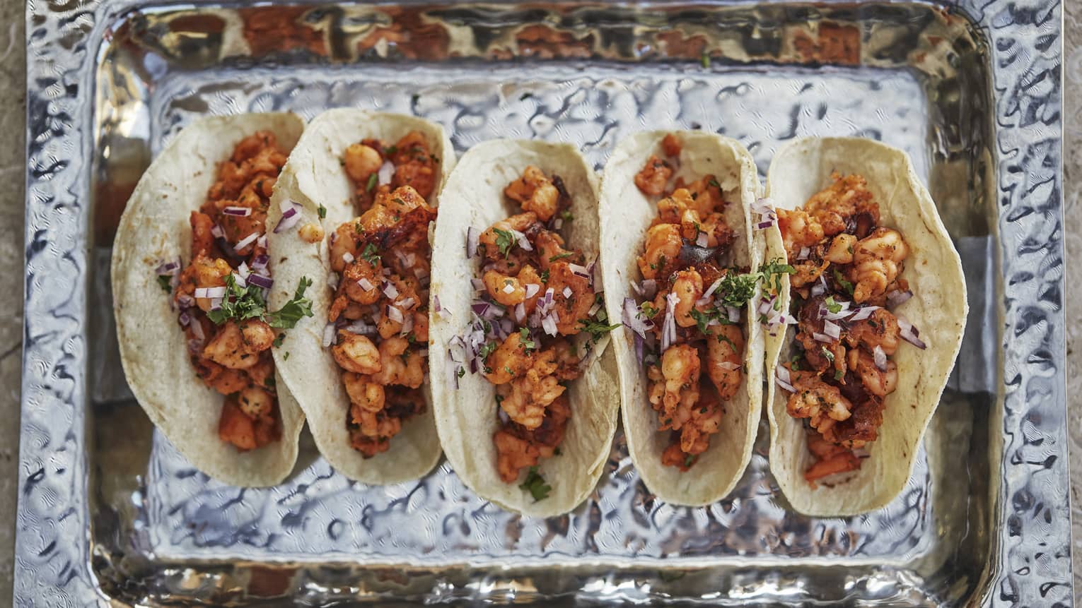 Aerial view of row of five tacos in dish