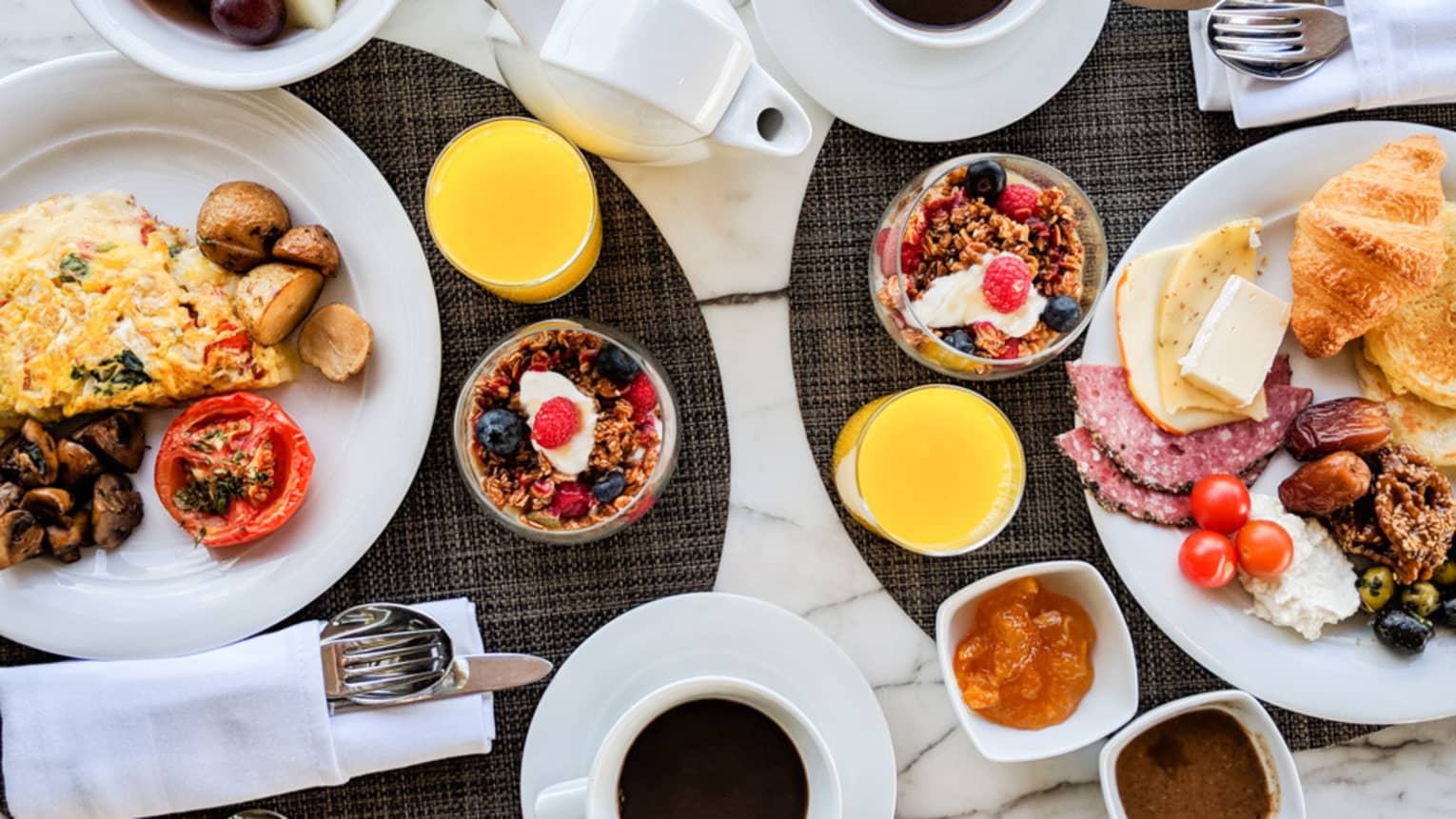 Aerial view of brunch table with omelette, cheeses, meats, croissants, cups of granola and yogurt