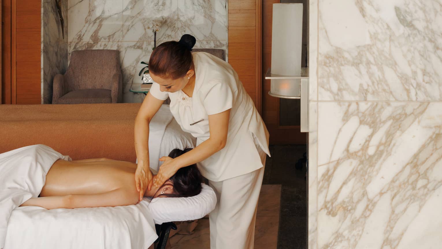 A female spa therapist performing a massage on a woman, face down on spa treatment table, in a chic luxury spa with marble walls