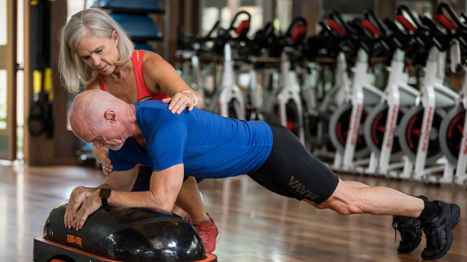 Fitness trainer helps man balance on pilates board in exercise studio