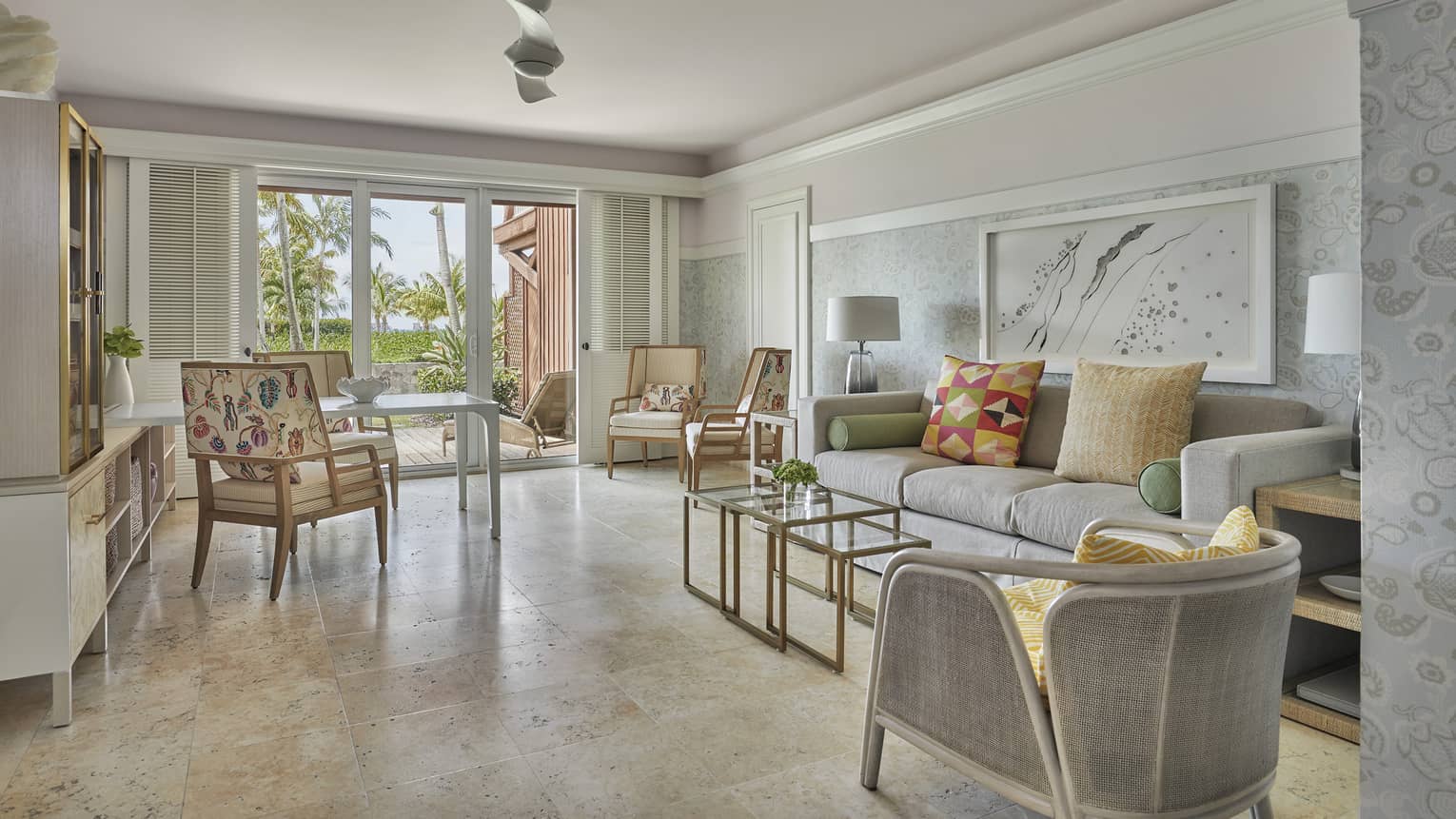 Airy living room, with tan floors, light grey sofa, arm chair, walk-out patio
