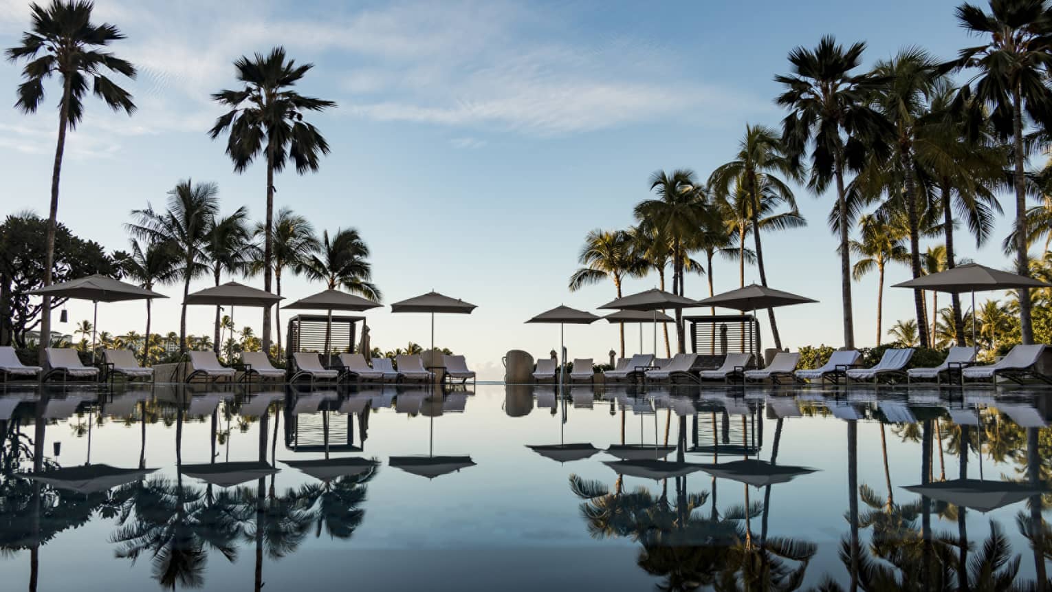 Large pool reflecting the palm trees and lounge chairs around it