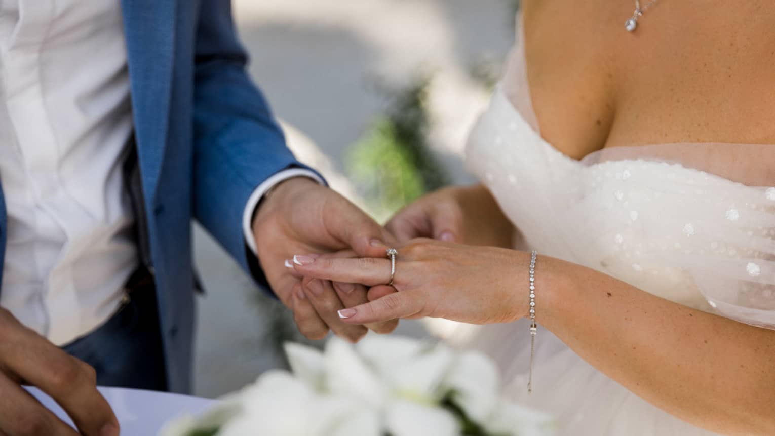 Closeup of groom in blue tuxedo placing ring on bride?s finger