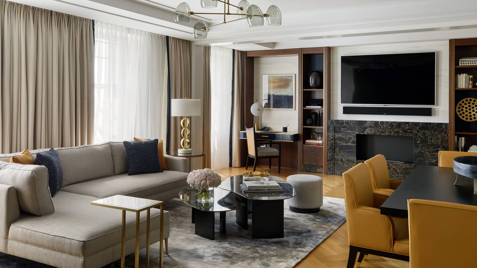 L-shaped grey sofa by coffee table, large TV over fireplace, dining chairs