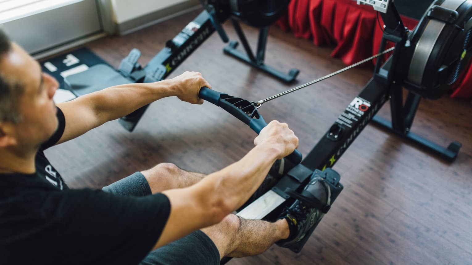 Man sits, pulls handle of cardio rowing machine in fitness facility