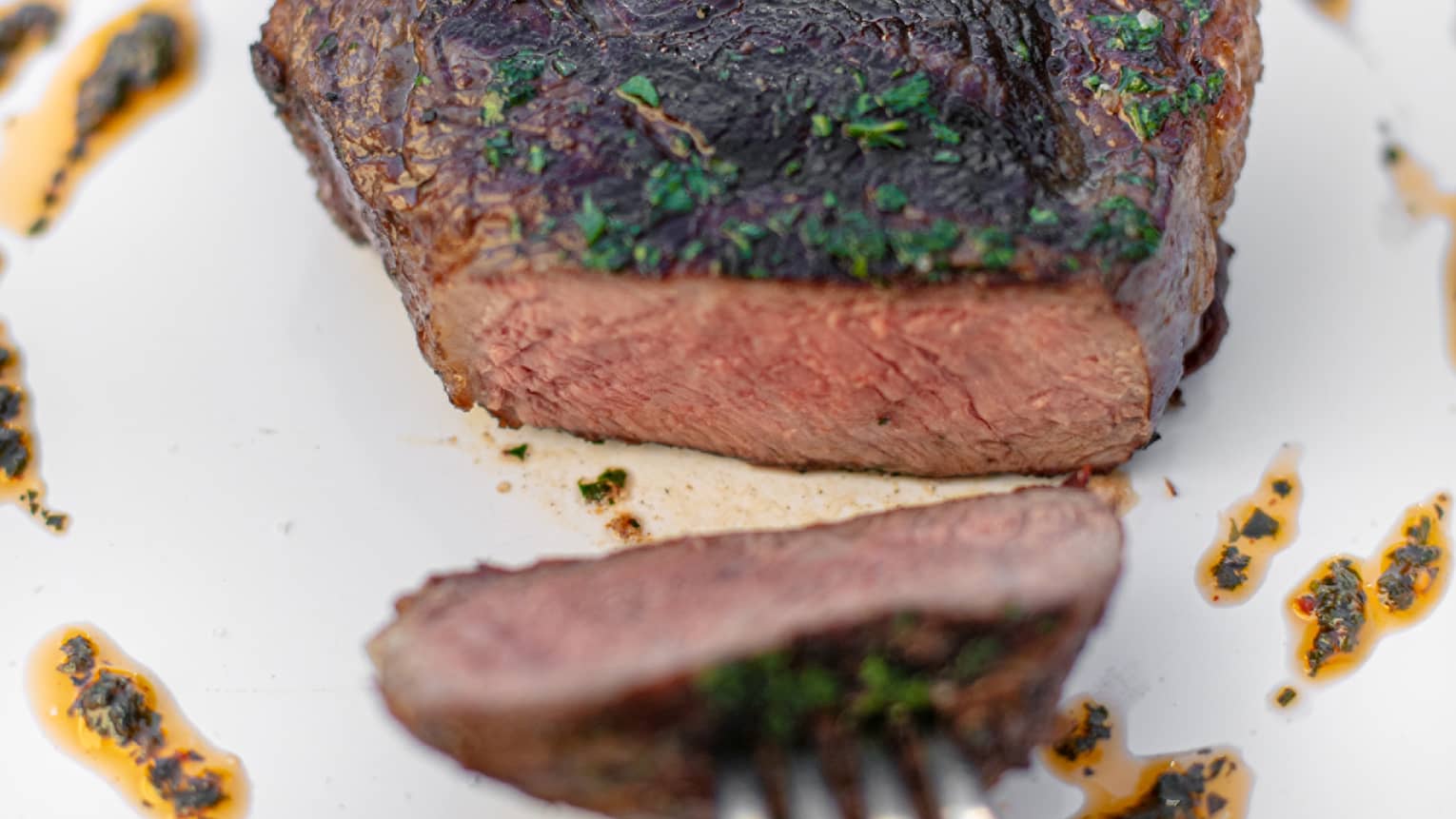 A fork pulling a piece of sirloin across a plate.