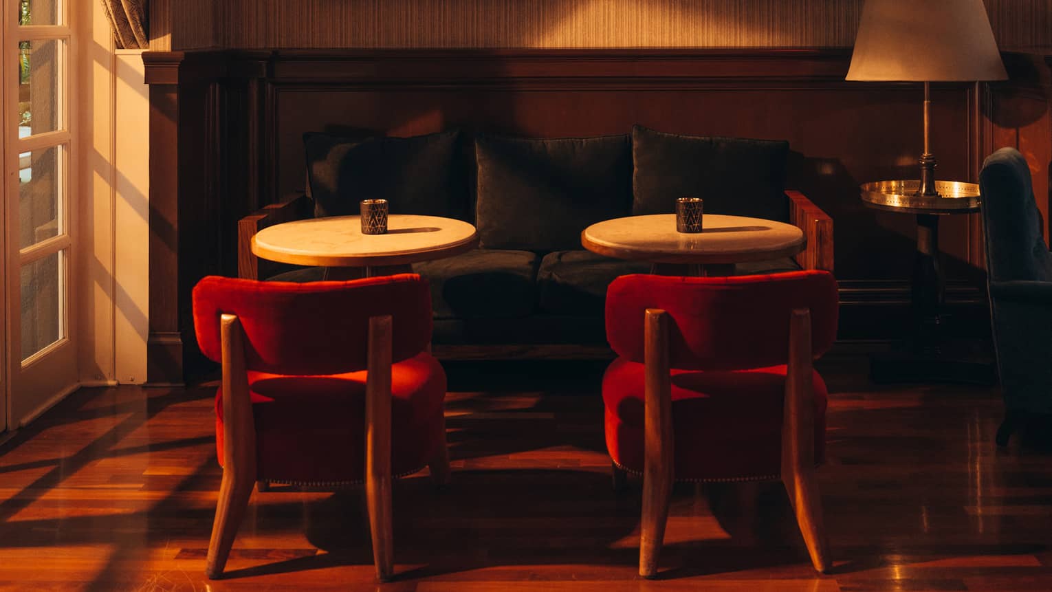 Couch with two tables and two red chairs in front of it, and picture frames on the wall in the background.