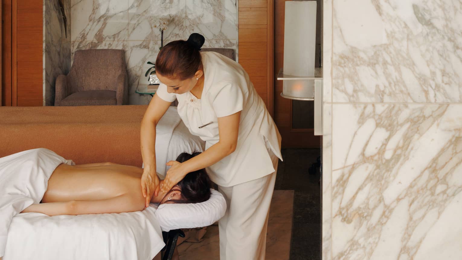 A female spa therapist performing a massage on a woman, face down on spa treatment table, in a chic luxury spa with marble walls