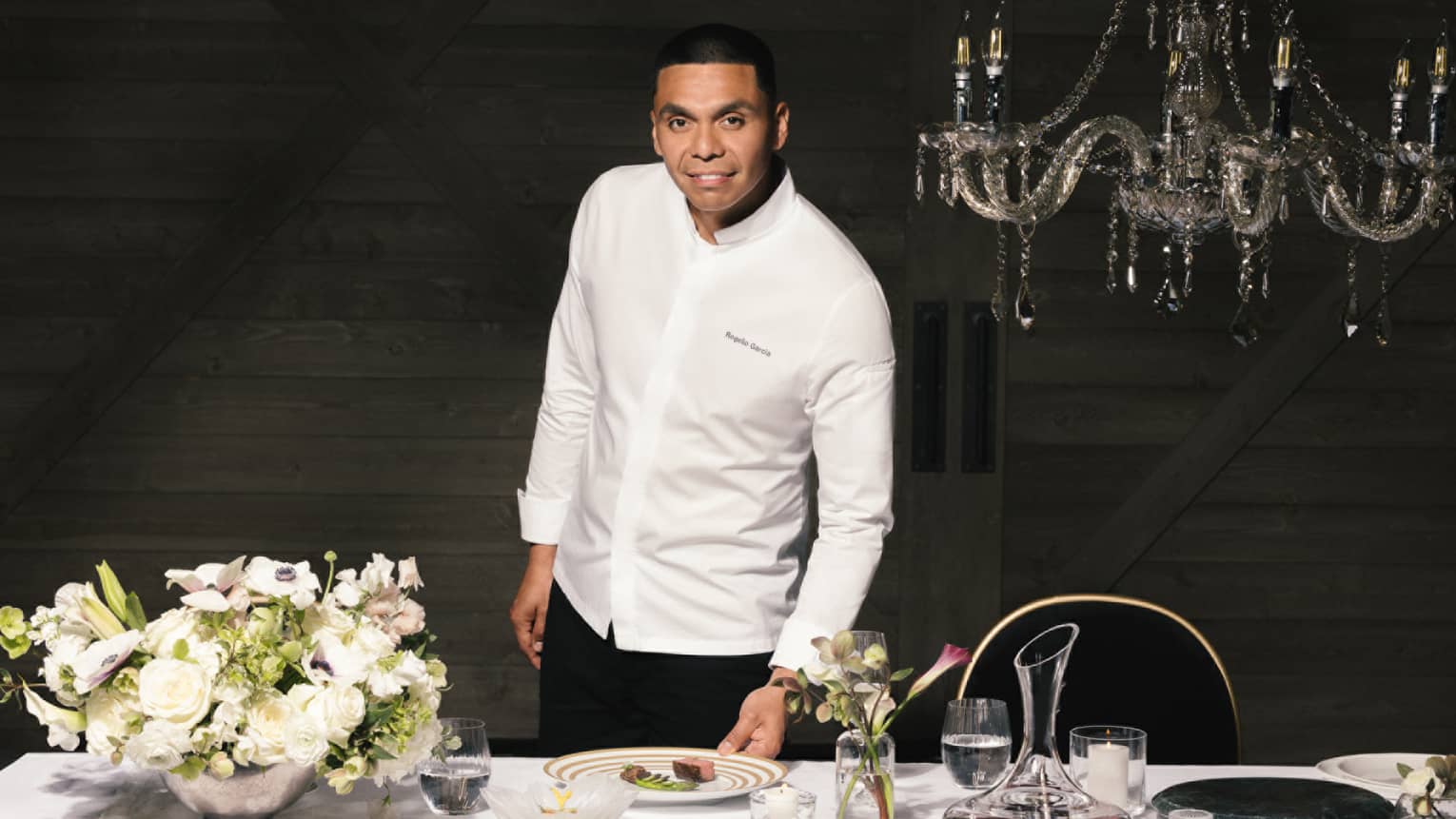 Chef Rogelio standing near a dining table with a bouquet of flowers on the table and place settings.