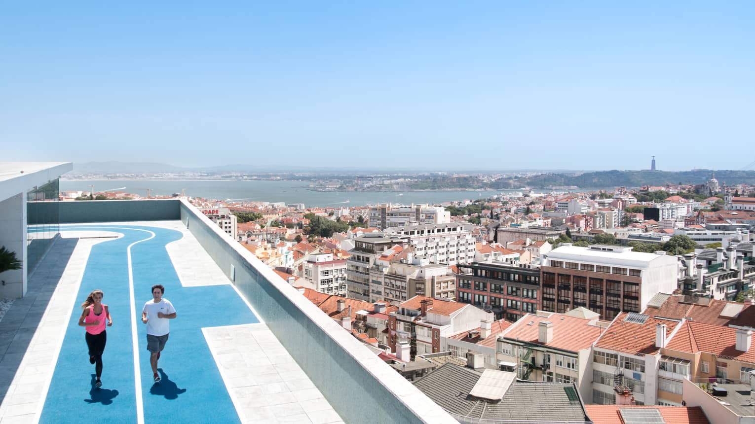 Two people run on blue, rooftop running track, overlooking Lisbon