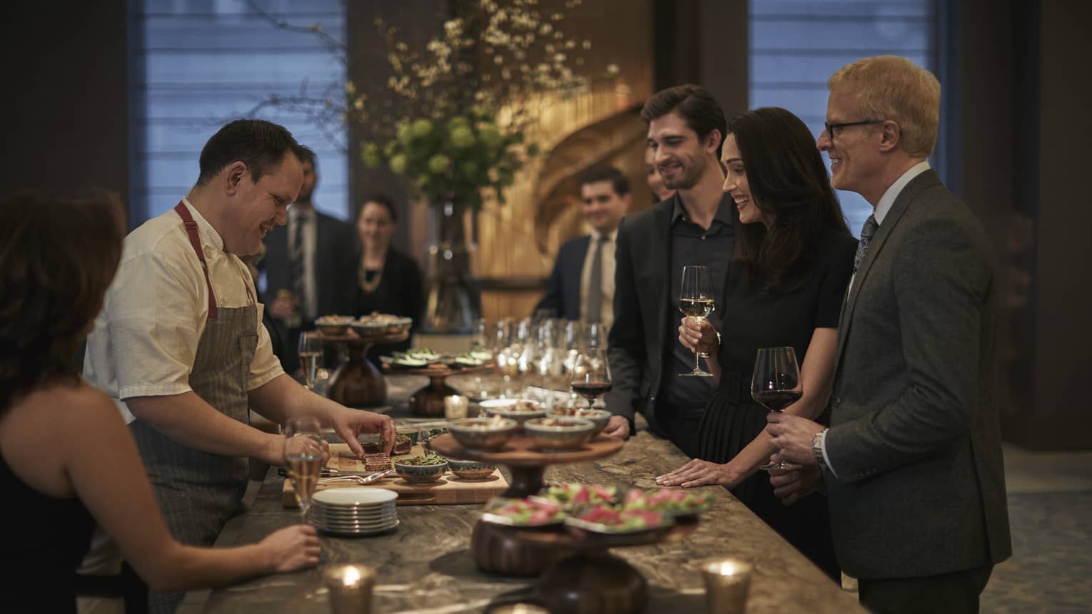 Culinary team and group examine, taste menu and wine at long buffet table