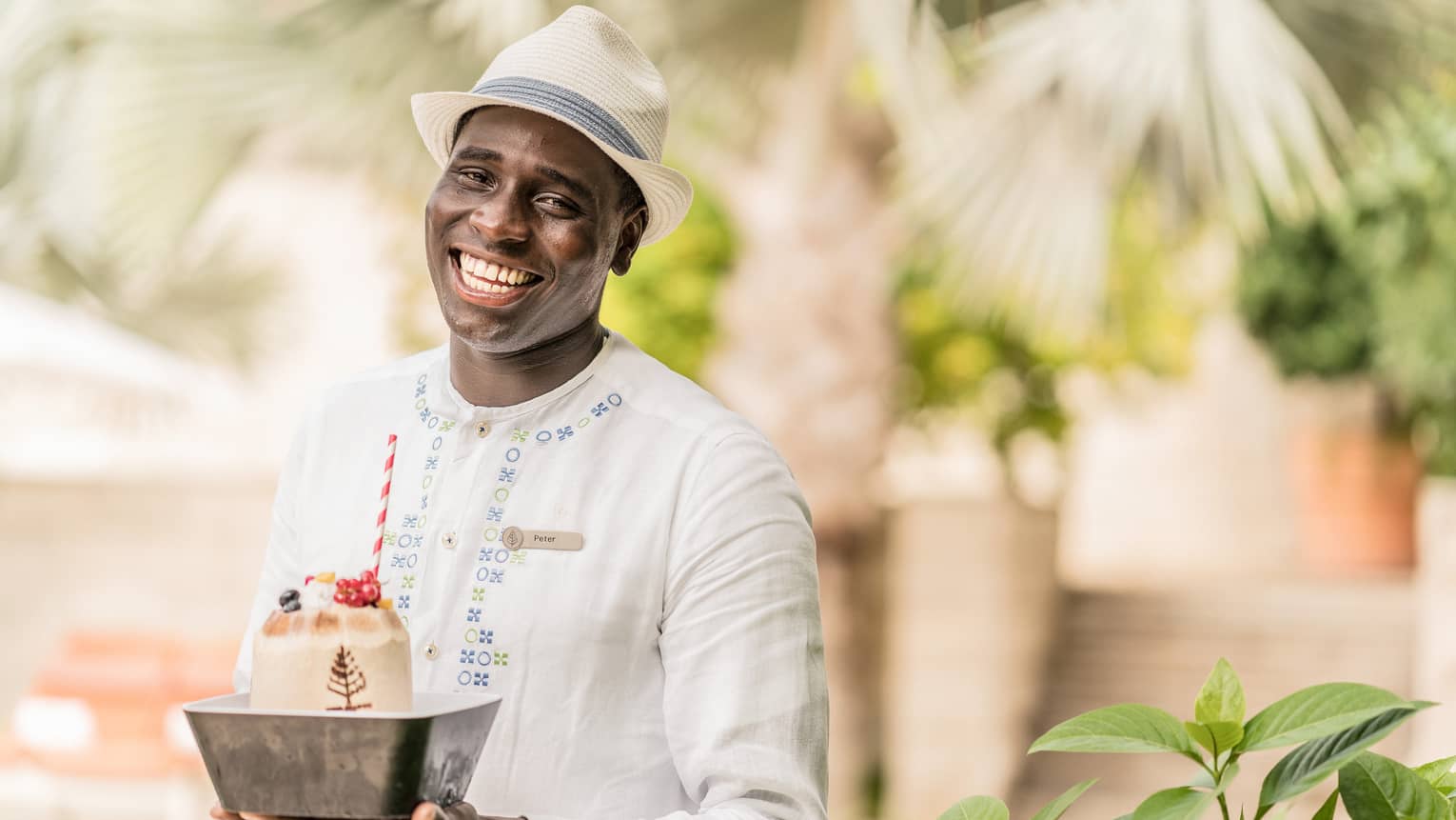 Pool staff member in white tunic and fedora holding ice cream dessert with striped straw