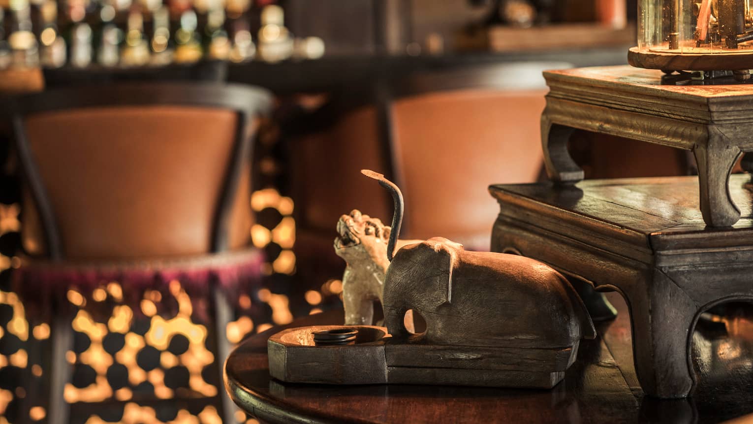 Close-up of elephant carvings on wood table. Burma Bar stools in background