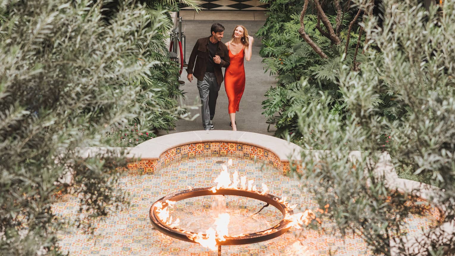 A woman and man walking in a courtyard surrounded by plants and a small fountain.