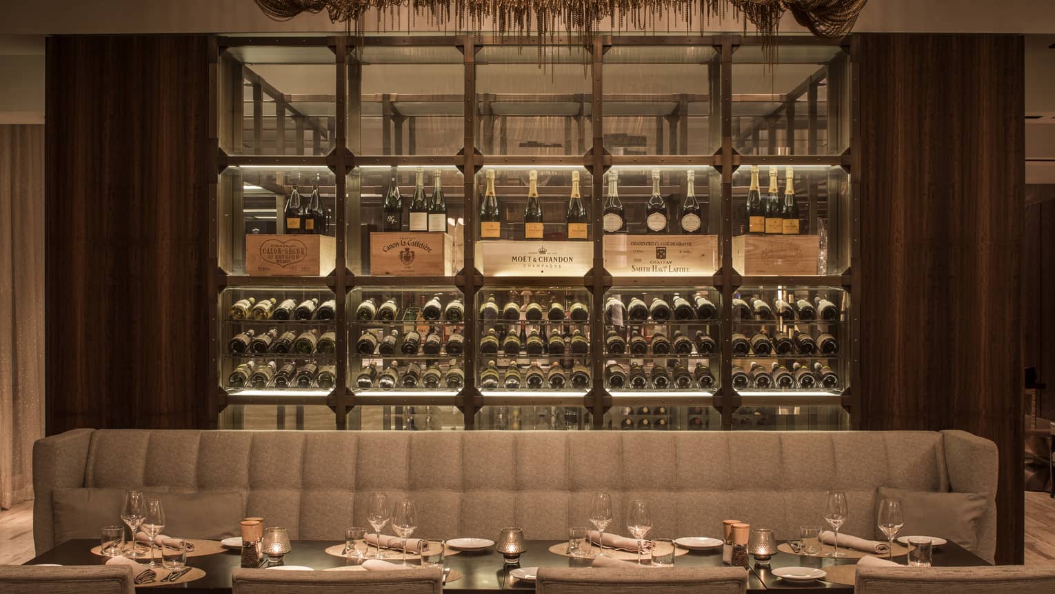 Long beige banquette along dining set dining table with glassed wine cellar in back