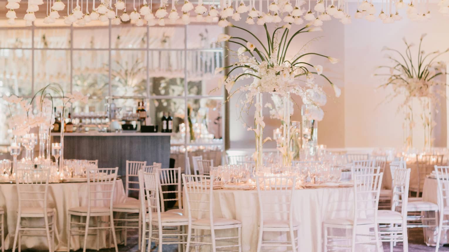 A reception area with tables, hanging lights and a bar in the back of the room.