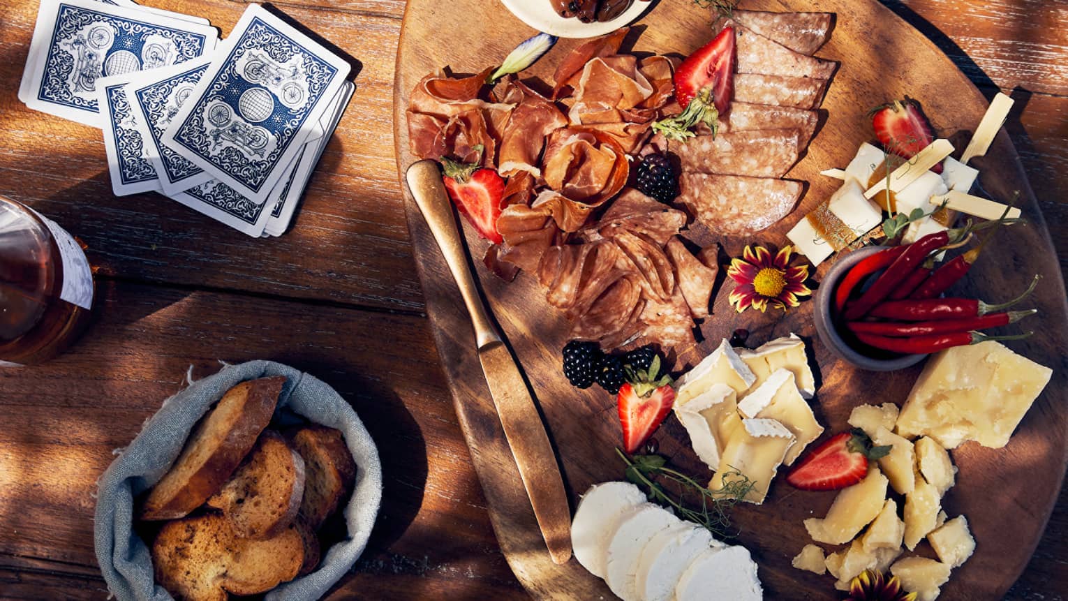 An assortment of cheese and bread and drinks on a table with playing chards.