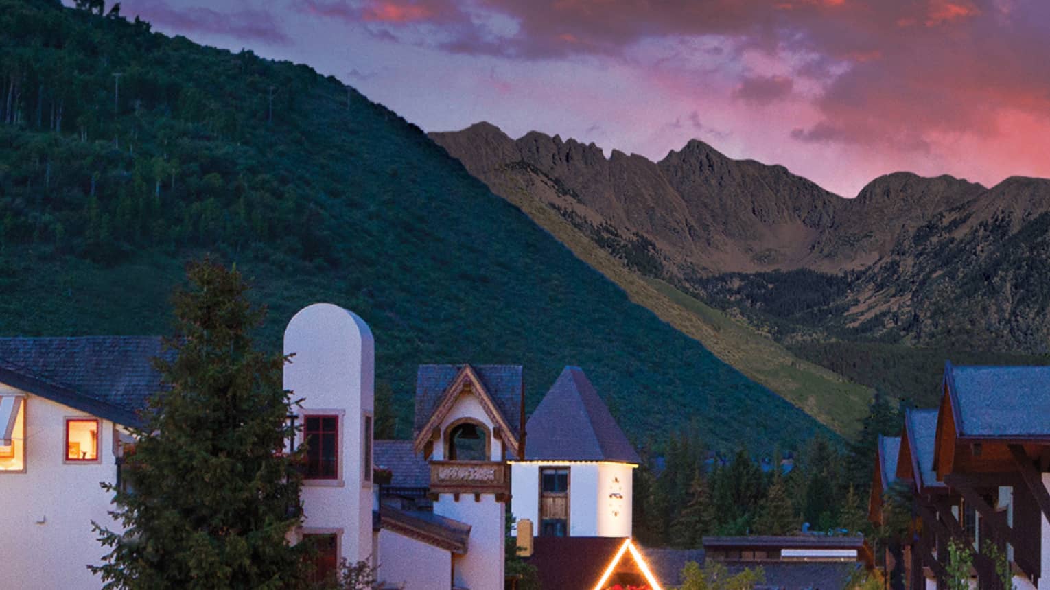 A sunset over a small village like city center with white buildings and mountains in the distance.