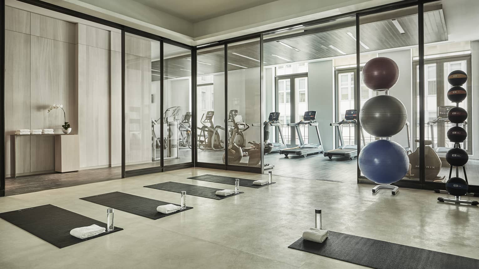 Yoga mats and water bottles in rows on Fitness Centre flow, stack of pilates balls