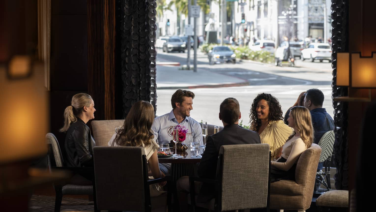 A group of people sitting around a large round table with a view of a road outside.