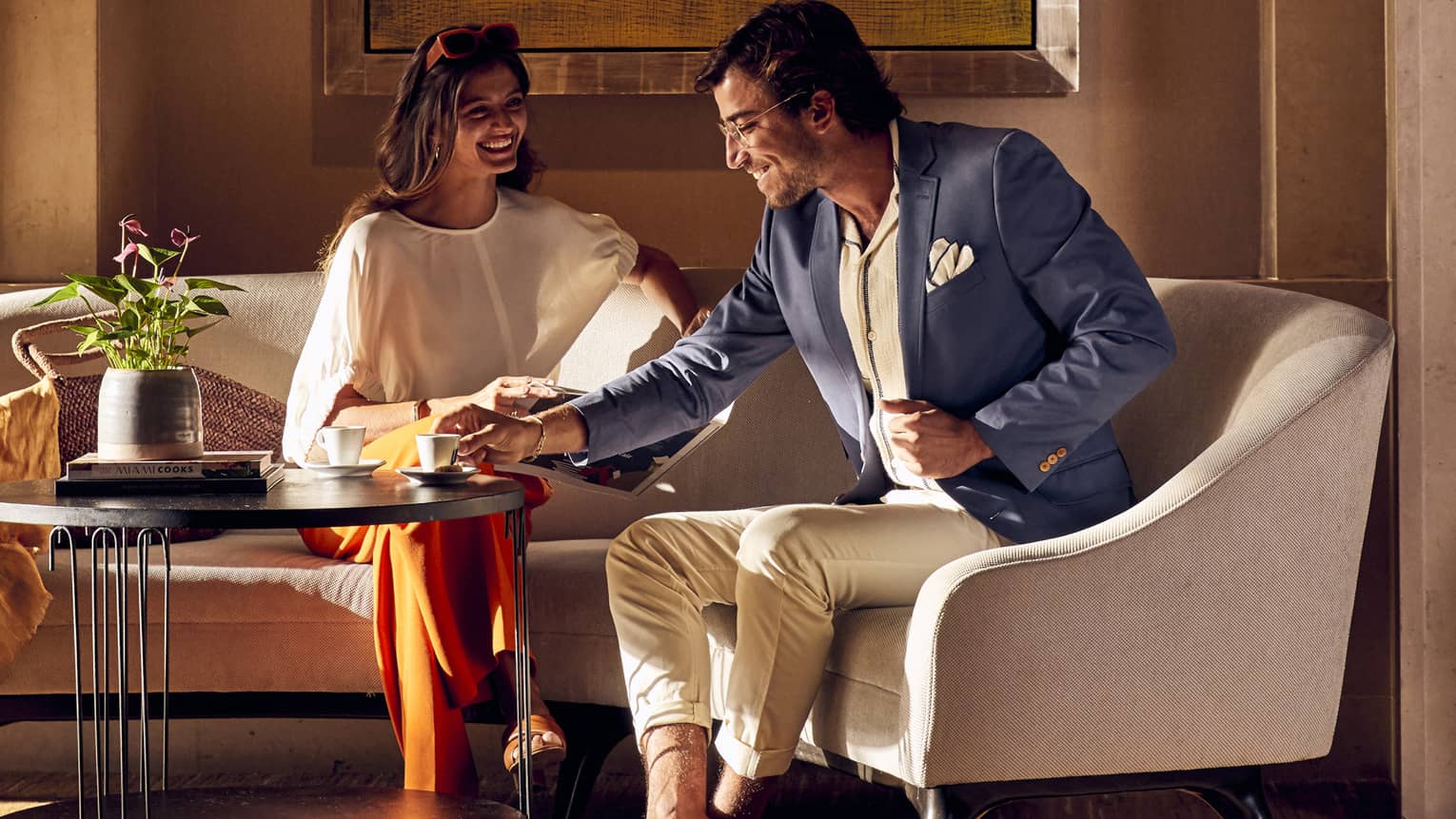 A man and woman enjoying coffee while sitting on a sofa.
