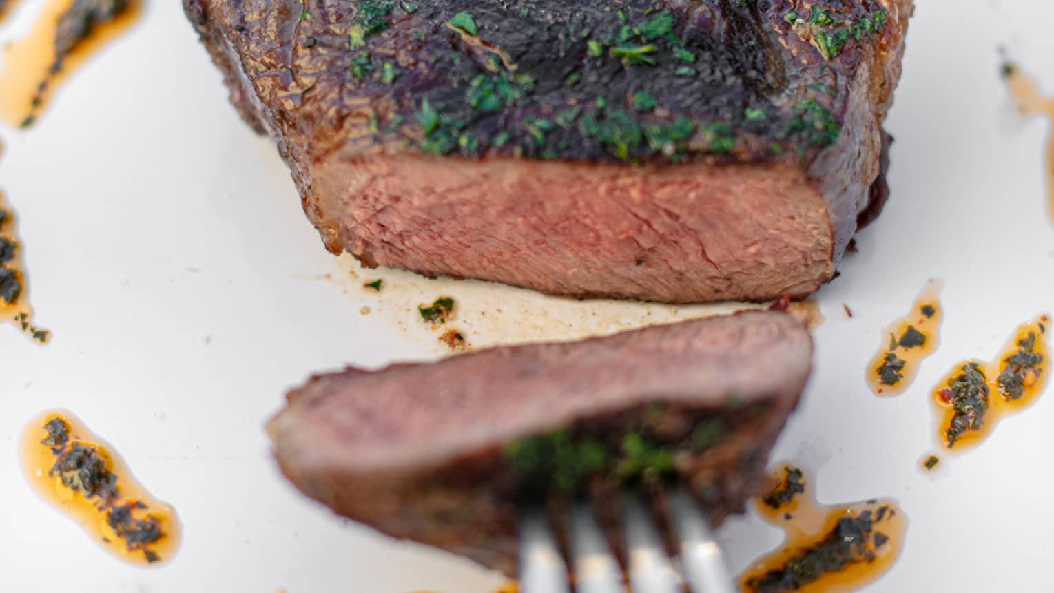 A fork pulling a piece of sirloin across a plate.