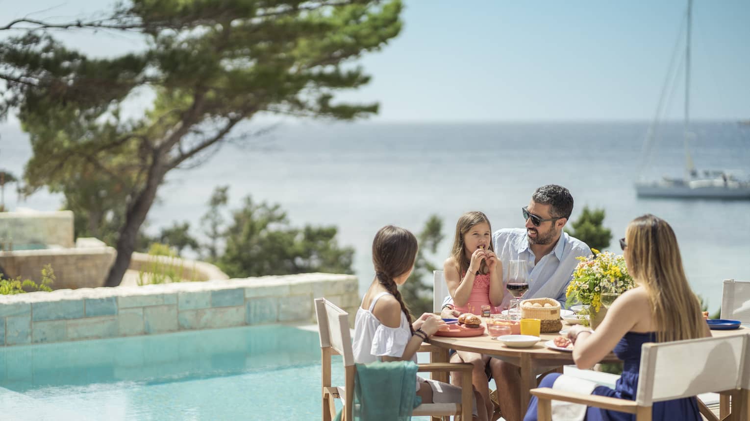 Family of five enjoys a meal outside next to the plunge pool, a sailboat on the Mediterranean in the background