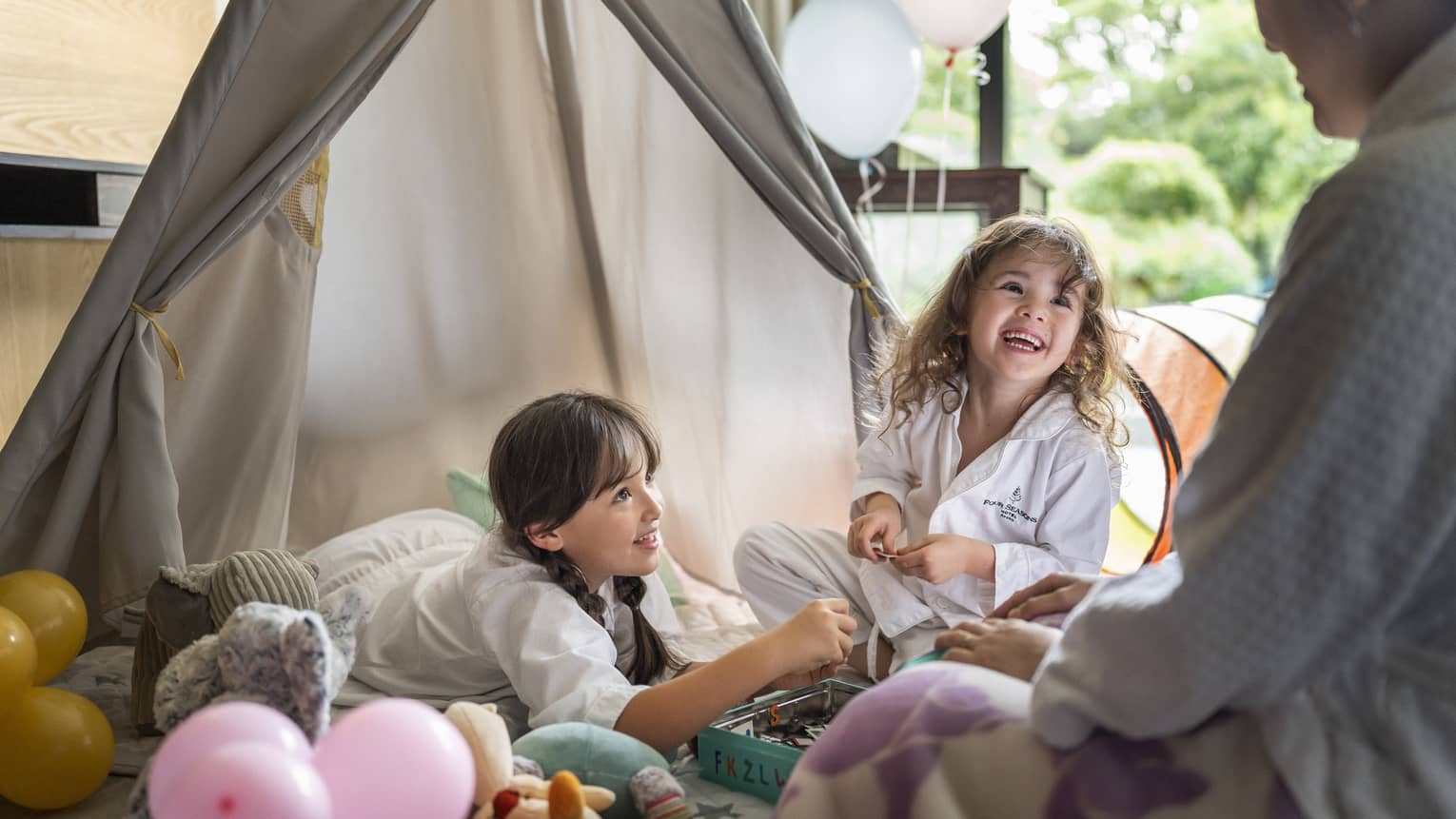 Mother and two young daughters in match white bathrooms share a laugh in the kids tent