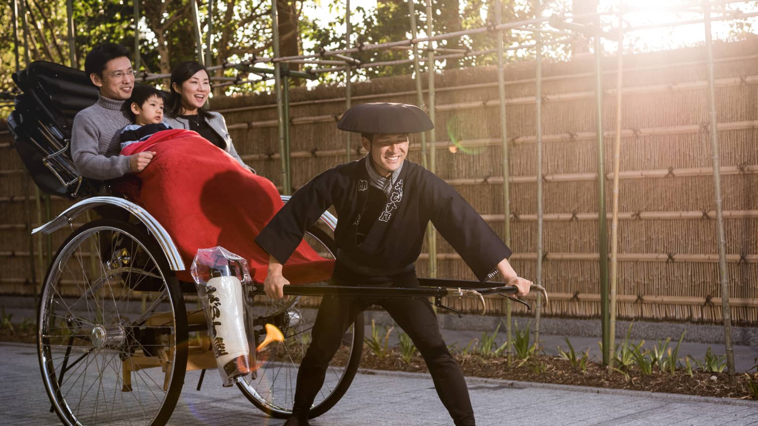 Couple, young boy under red blanket ride in rickshaw wagon pulled by man