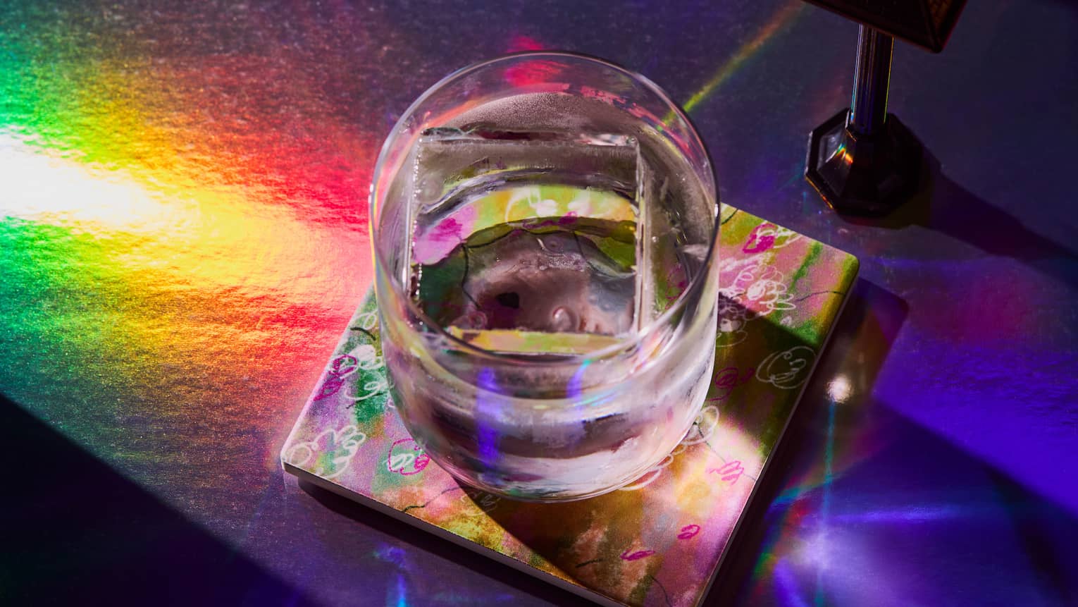 A cocktail sitting on a table, lit by colourful lights,A cocktail sitting on a table, lit by a rainbow of light