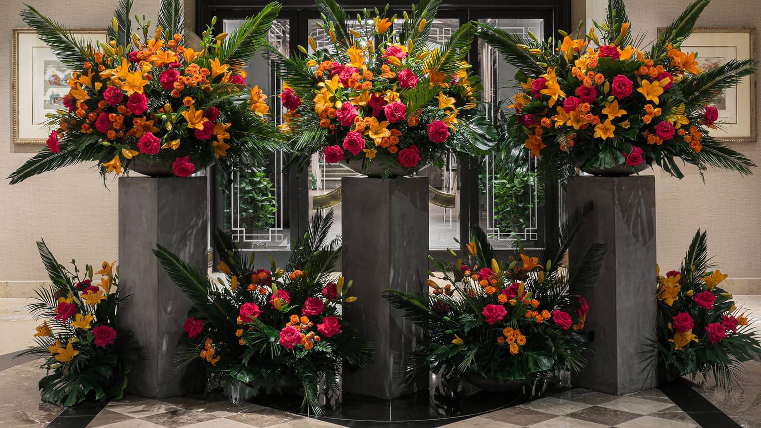 A bright, spacious, neutral-toned lobby area is decorated with elegant, artistic floral arrangements of red, orange and green.