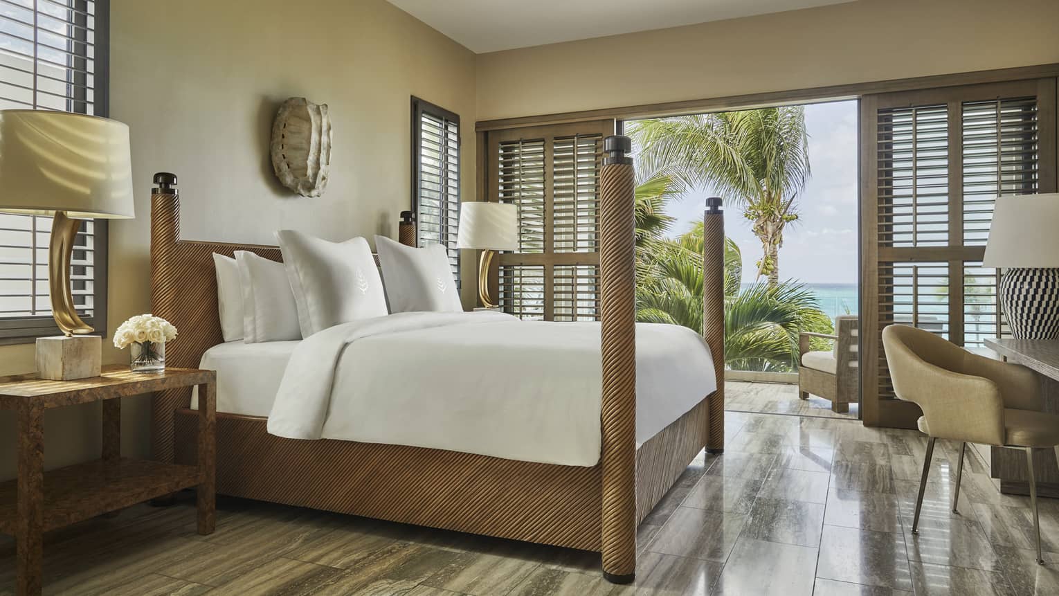 Bright bedroom with four-poster bed, wood accents and balcony view of palm trees and ocean.