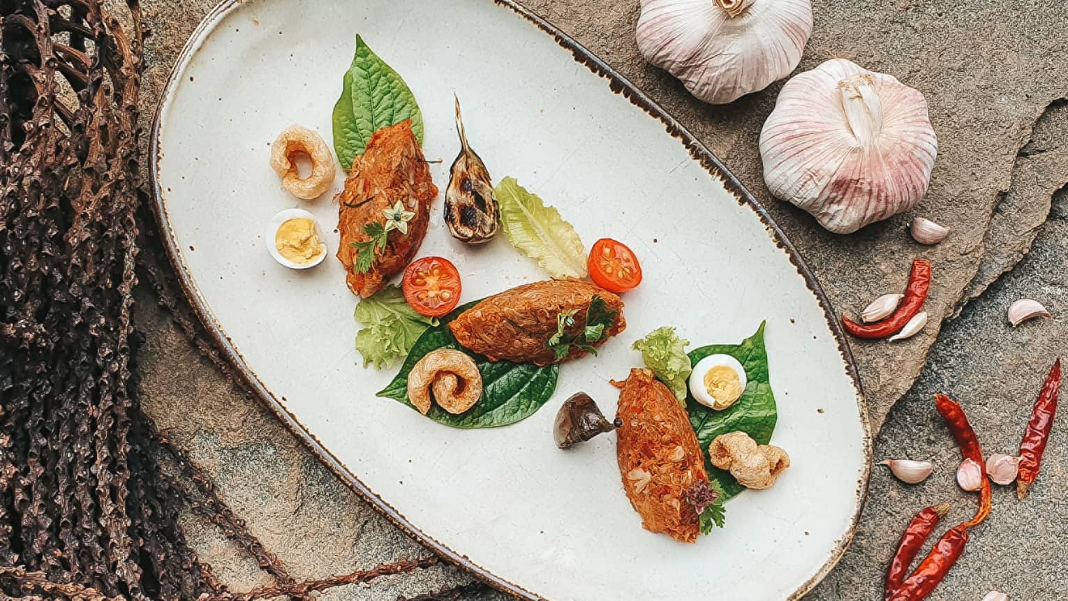 Signature Dish Jackfruit Curry Dip on an oblong plate, whole garlic bulb and red chilli garnishes