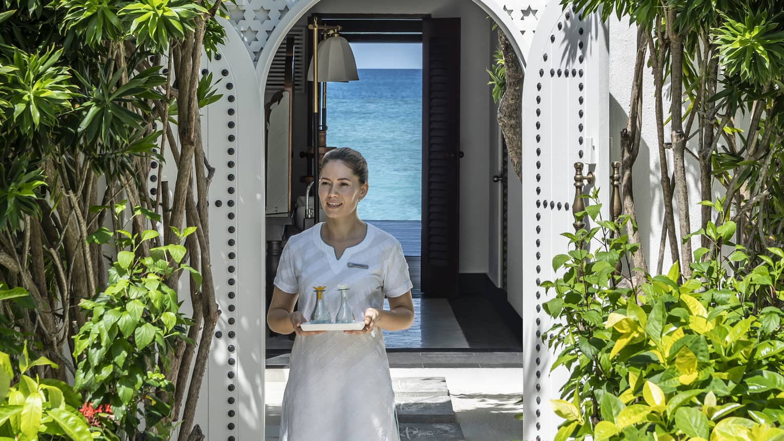 A four seasons spa member carries a tray of food through a shrubbery lined archway 