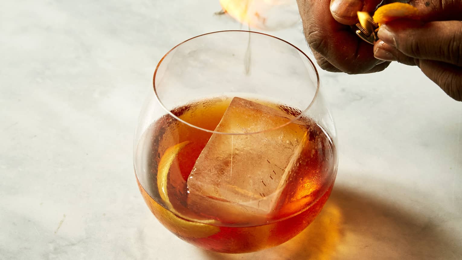 Hands hovering over a bronze cocktail in a clear glas sitting on marble counter