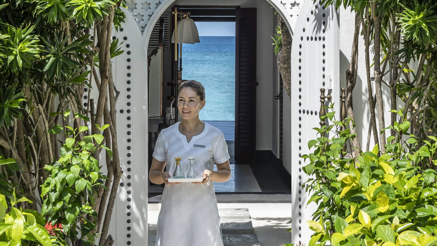 A four seasons spa member carries a tray of food through a shrubbery lined archway 