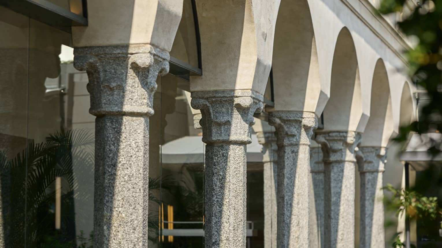 A row of stone arches on an old building, potted plants are placed under the arches.