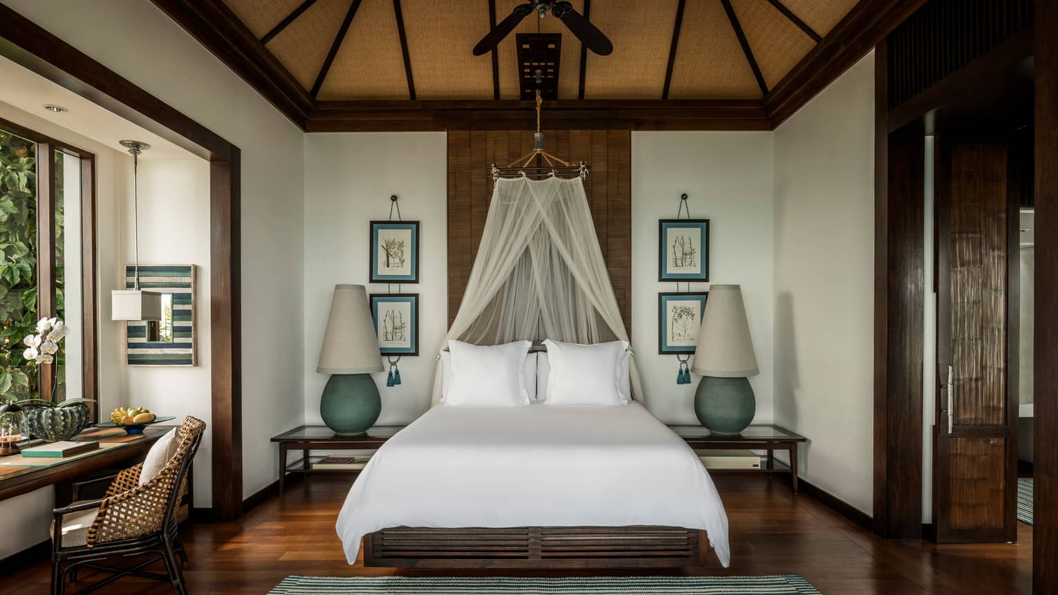 Family Pool Villa bed with white net canopy, large lamps on each side, wood floors, desk by window