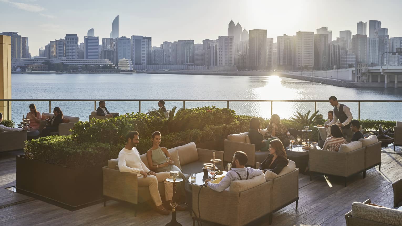 People mingling on sofas of outdoor terrace, overlooking sea and Abu Dhabi city