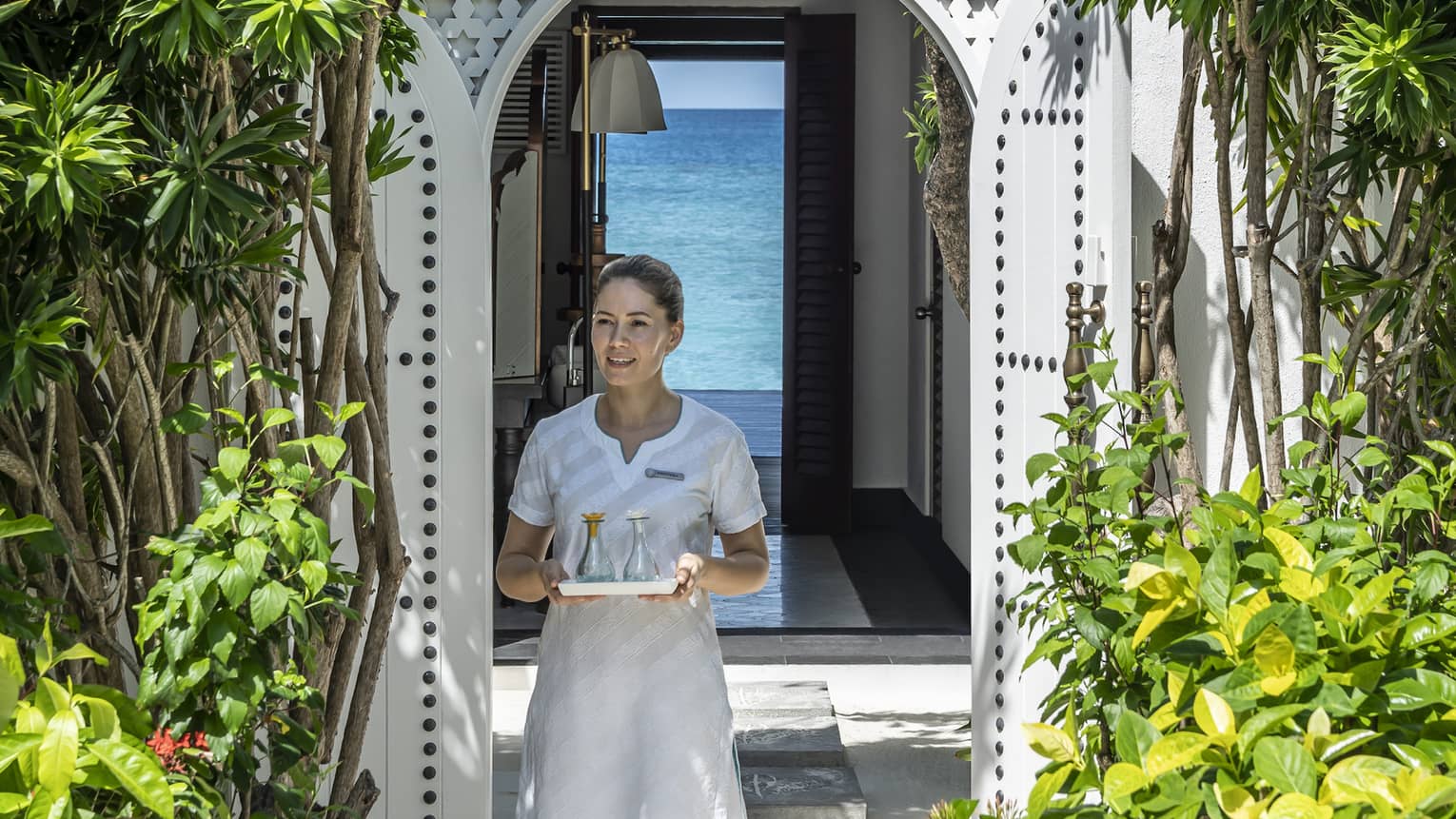 A four seasons spa member carries a tray of food through a shrubbery lined archway 