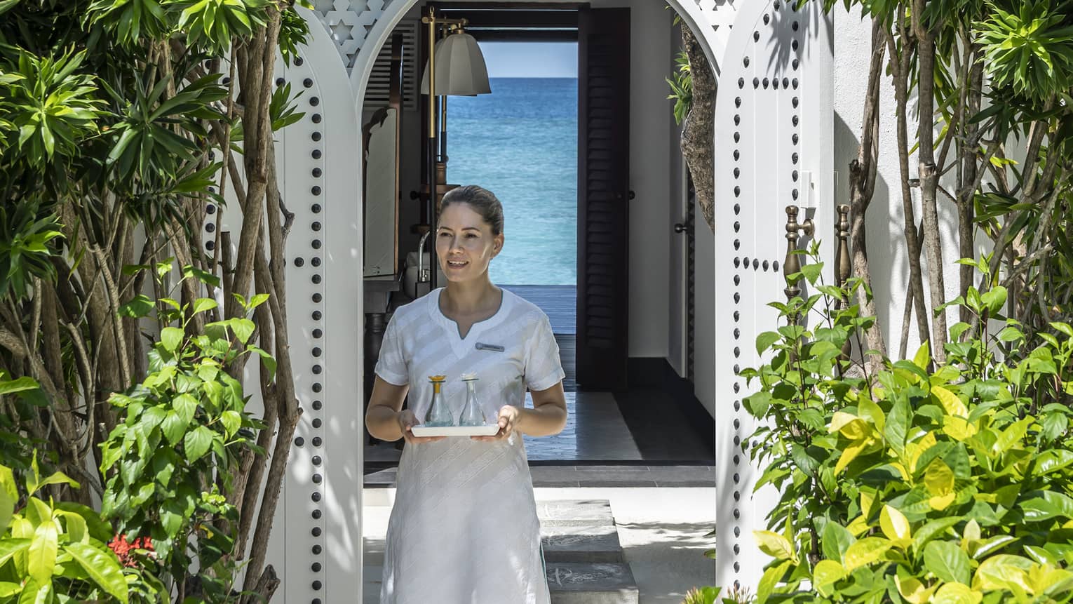 A four seasons spa member carries a tray of food through a shrubbery lined archway 